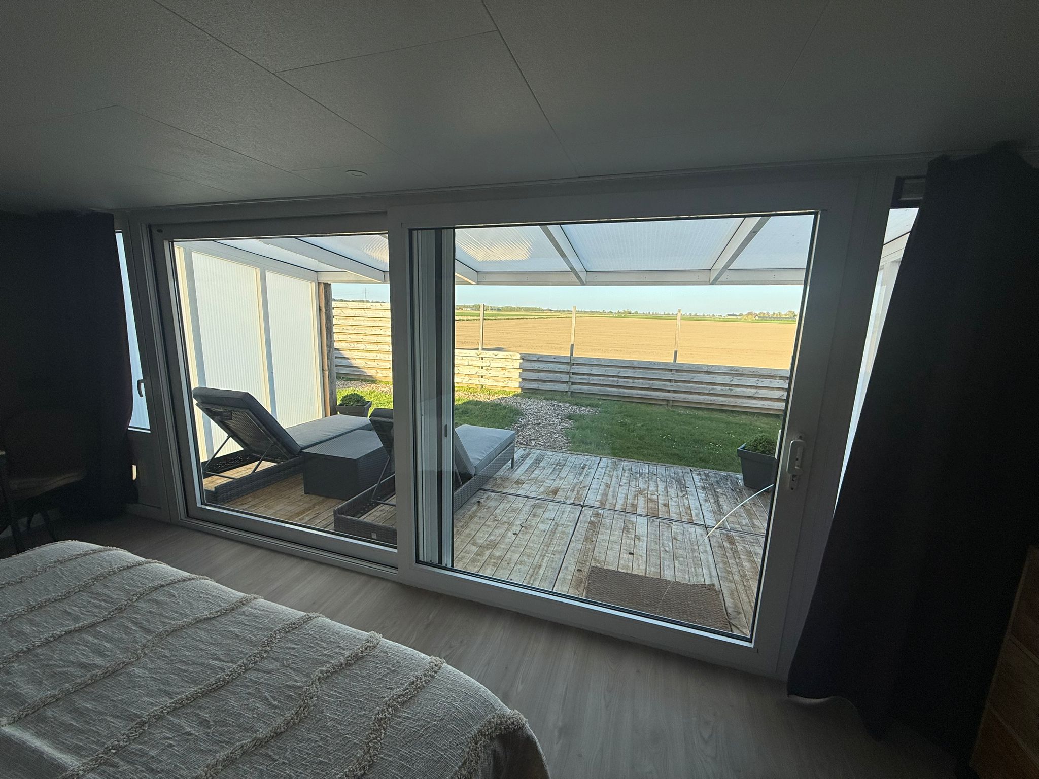 Uitzicht door de glazen pui op het terras met ligbedden en de weidse landerijen