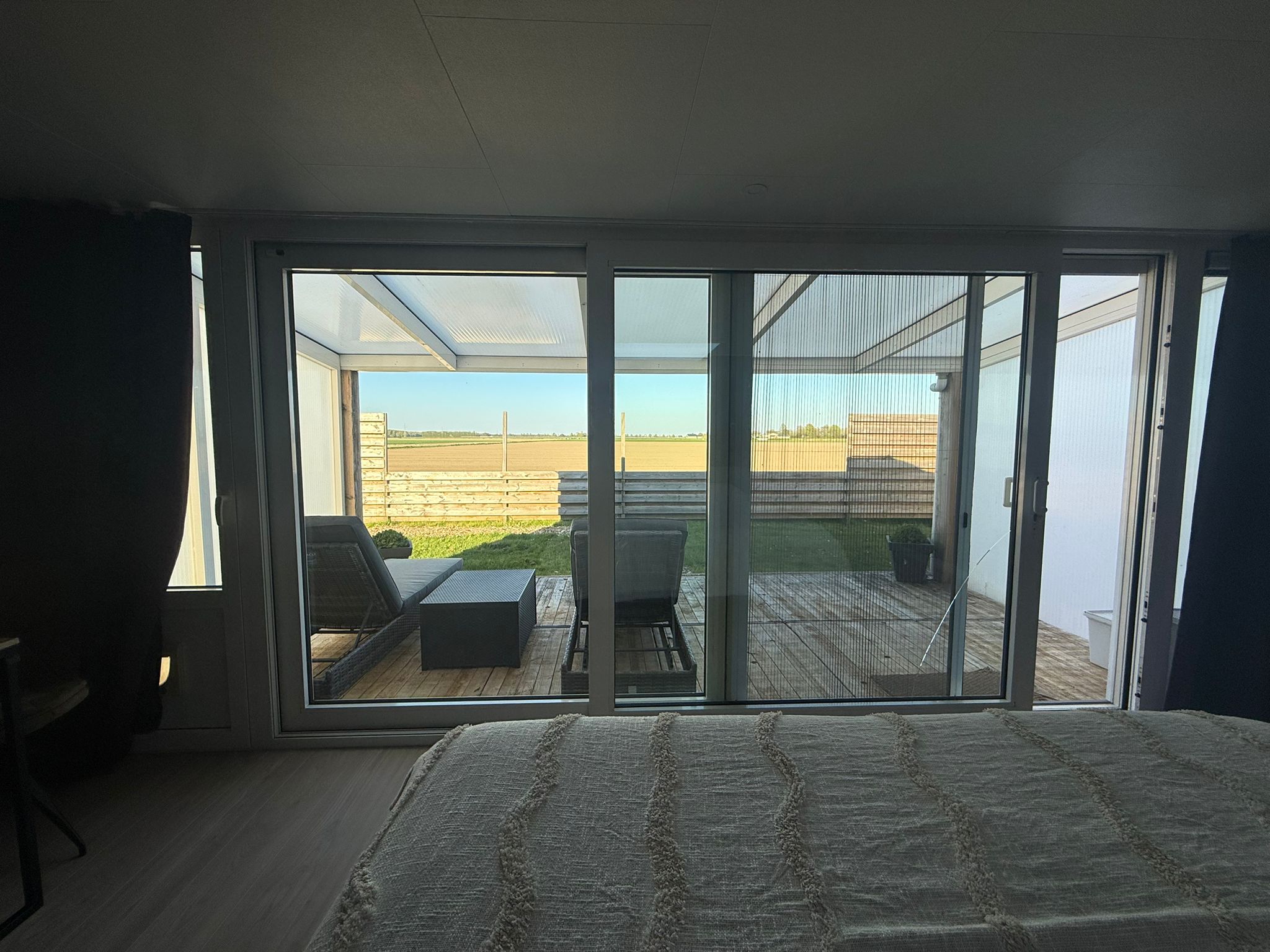 Zicht vanuit de slaapkamer door de schuifpui op het overdekte terras en de landerijen